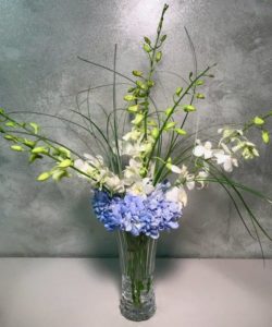 bouquet of white dendrobium orchids, blue hydrangea with a touch of glitter and bear grass in a cut glass vase b
