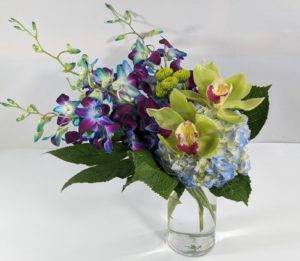 Exotic blue dendrobium orchids are paired perfectly with blue hydrangea, a little lime green hypericum adds a pop to the blue. Hand-designed in a clear glass vase and delivered to someone special in your life!