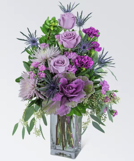 This jewel of an arrangement will brighten anyone's day! Wild Amethyst contains roses, spider mums, kale, carnations, dianthus, and a variety of foliage displayed in a tall clear vase. This stunning piece will make any home or office sparkle. We want you to have the very best. Substitutions may be made based on availability and quality of product. We will always maintain the integrity of the design. Please call our shop directly if you have questions.